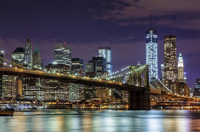 Downtown Manhattan and the bridge's cables lit, seen across the East River at night