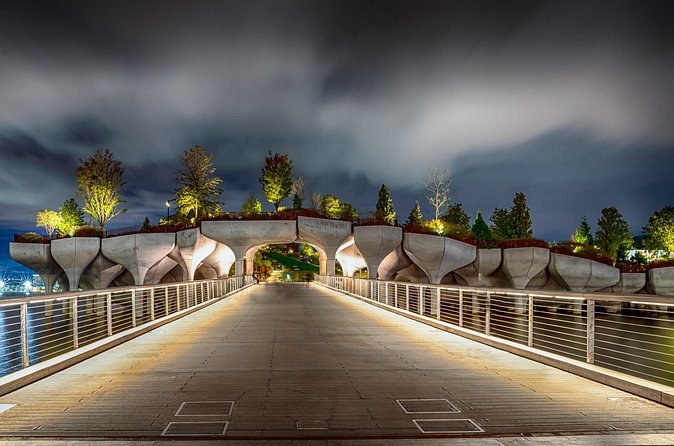 A park raised on concrete tulip piers in the Hudson, its walkway lit at night