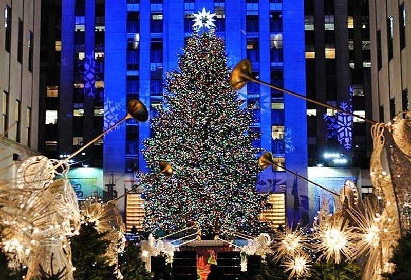 The Christmas tree at Rockefeller Center lit in front of a tower washed in blue