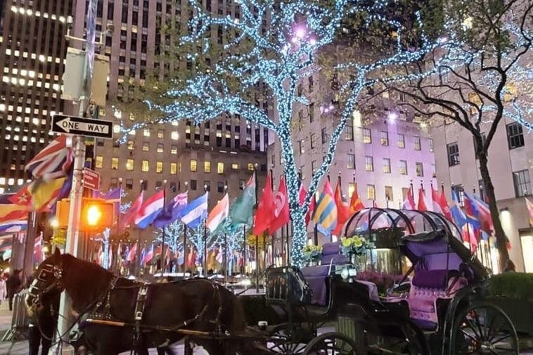 Flags and white tree lights around the plaza at Rockefeller Center after dark
