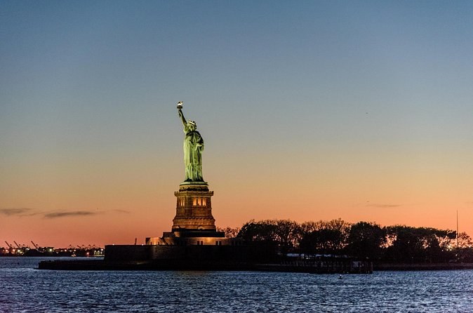The Statue of Liberty in silhouette on its island against an orange sunset