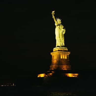 The Statue of Liberty floodlit gold on its pedestal against a black sky
